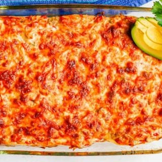 A cheesy casserole with chicken and tortillas after being baked with cilantro and avocado slices on top