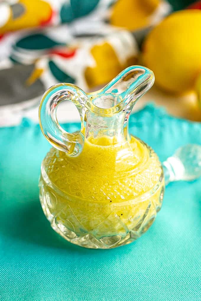 A yellow lemon vinaigrette in a small glass crystal jar on a turquoise napkin
