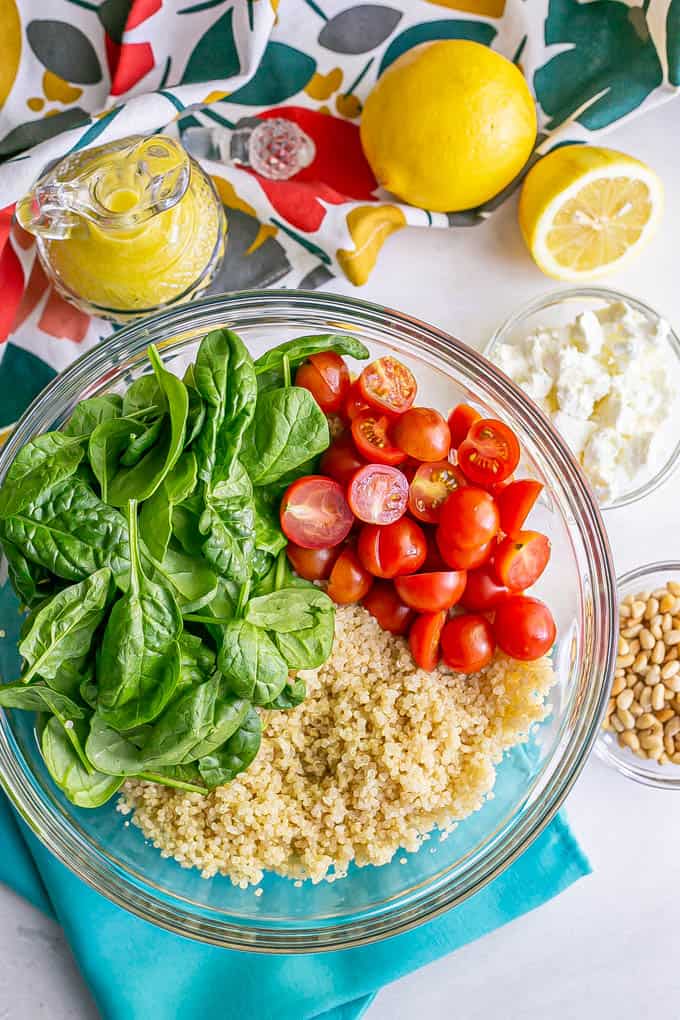 A bowl with quinoa, tomatoes and spinach and extra toppings and dressing in bowls to the side