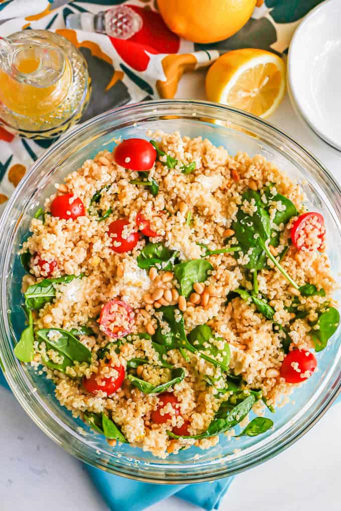 A large glass bowl with a quinoa spinach salad mix with lemon vinaigrette in a crystal jar to the side