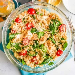 A large glass bowl with a quinoa spinach salad mix with forks to the side
