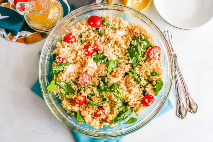 A large glass bowl with a quinoa spinach salad mix with forks to the side