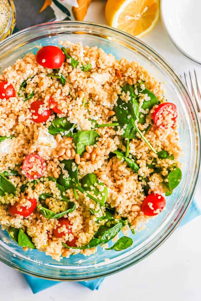 A large glass bowl with a quinoa spinach tomato salad mix with pine nuts on top