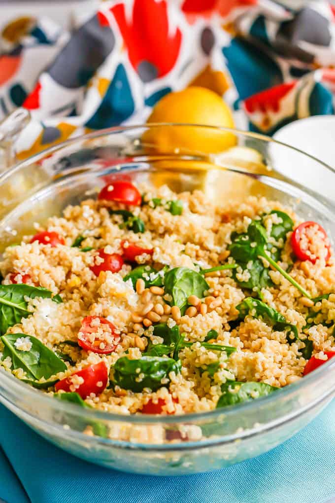 A large glass bowl with a quinoa spinach salad mix and lemons in the background