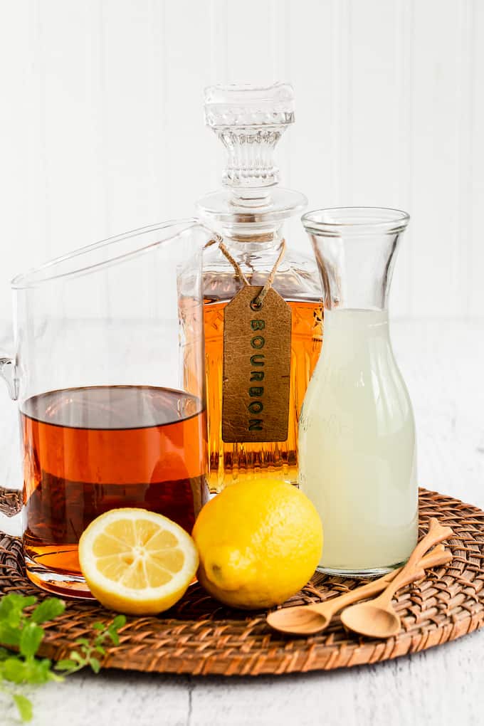 Drink ingredients to make a bourbon spiked Arnold Palmer drink laid on a circular woven mat