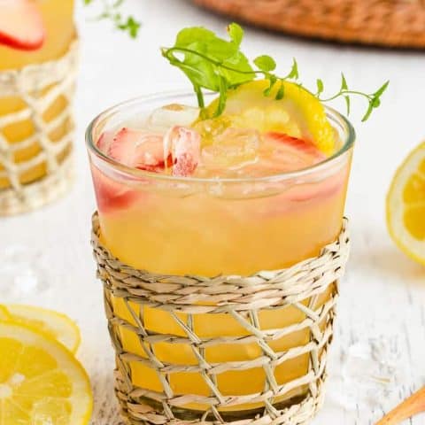 Close up of a spiked Arnold Palmer drink in a short clear glass with a woven glass holder around it and a small spoon nearby