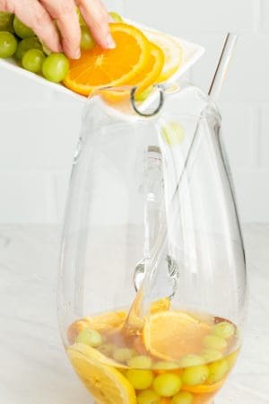 Fresh fruit being added to a large glass drink pitcher