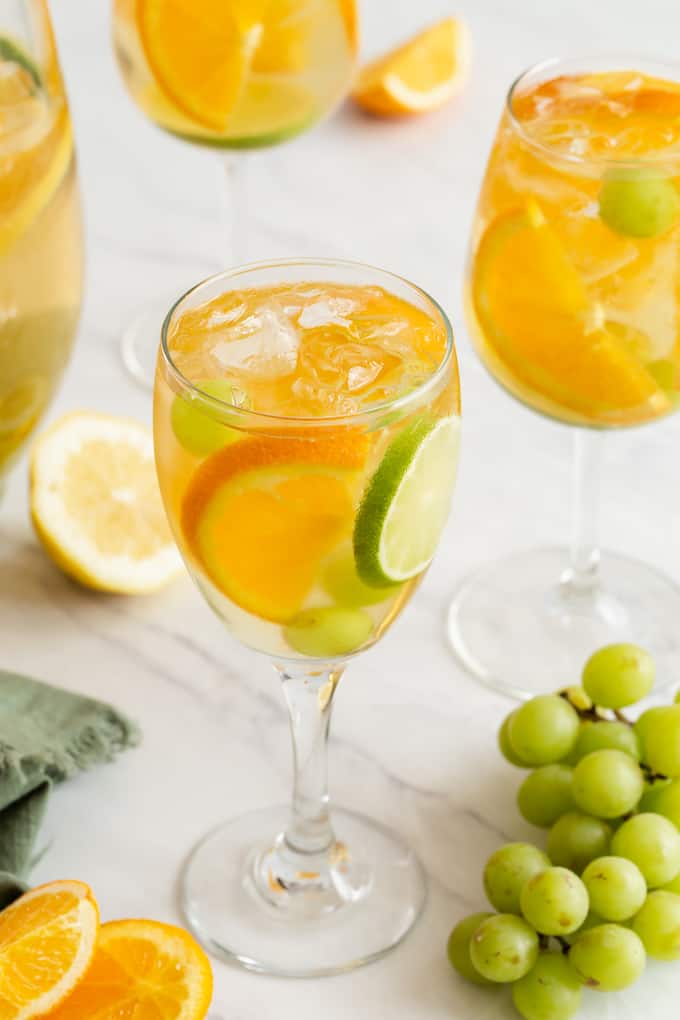 Two wine glasses filled with a sparkling white sangria, grapes, orange and lime slices