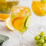 A wine glass filled with a white sangria, grapes, orange and lime slices with a text overlay on the photo
