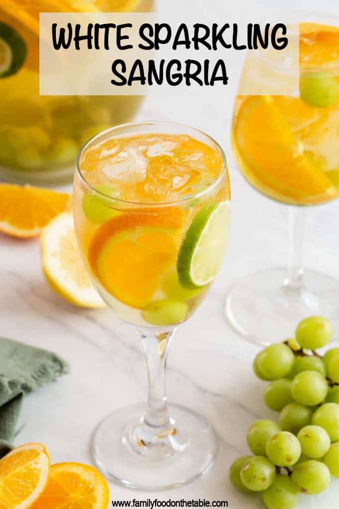 A wine glass filled with a white sangria, grapes, orange and lime slices with a text overlay on the photo