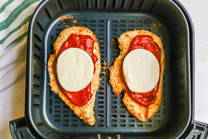 An Air Fryer with two chicken Parmesan cutlets with marinara and mozzarella before being cooked