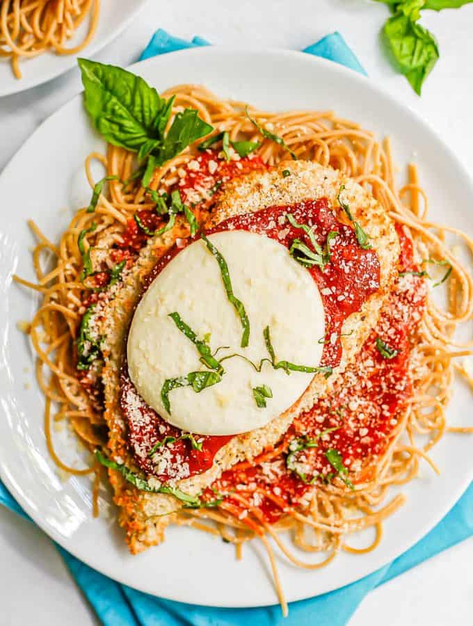 A breaded chicken cutlet topped with marinara and mozzarella cheese and basil served over spaghetti noodles
