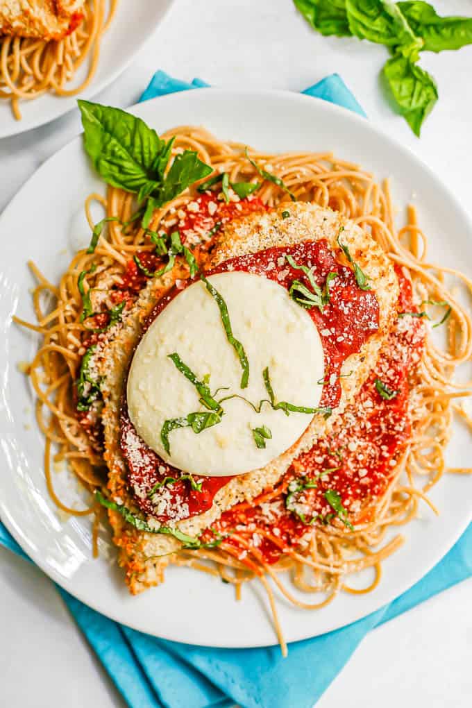 A breaded chicken cutlet topped with marinara and mozzarella cheese and basil served over spaghetti noodles