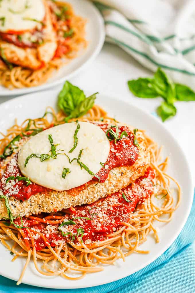Close up of a chicken Parmesan cutlet with marinara and fresh mozzarella on a bed of spaghetti