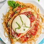A breaded chicken cutlet topped with marinara and mozzarella cheese and basil served over spaghetti noodles