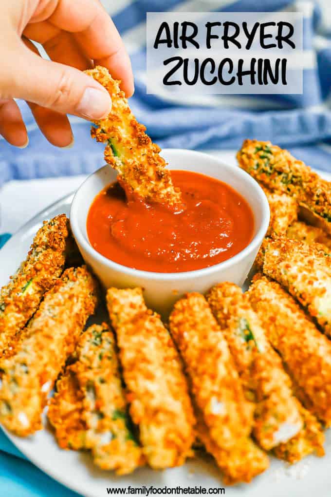 A hand dipping a crispy Air Fryer zucchini stick into a small bowl of marinara with a text overlay on the photo