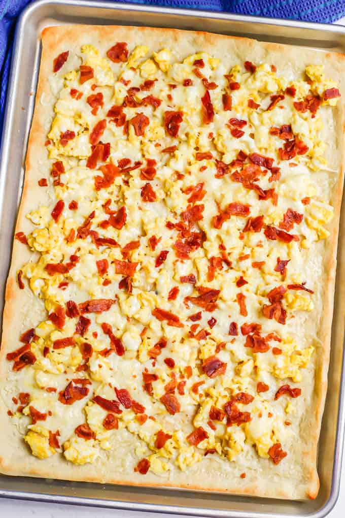 A cooked breakfast pizza on a sheet pan with scrambled eggs, bacon and melted cheese