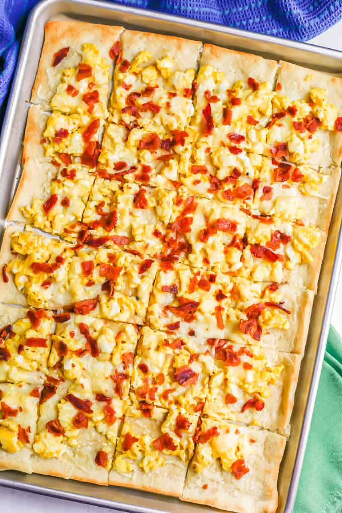 Overhead full shot of a sheet pan with a cooked pizza with scrambled eggs, bacon and cheese, cut into slices