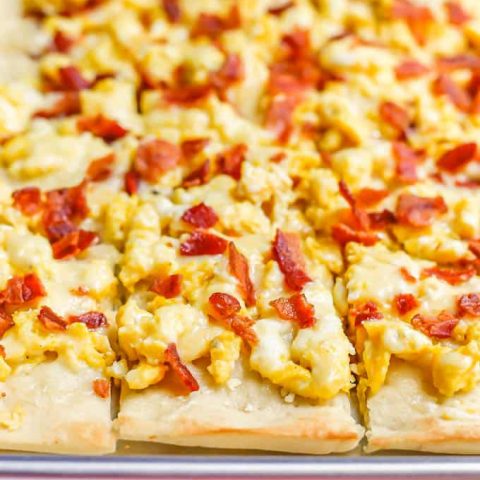 A sheet pan with a cooked pizza with scrambled eggs, bacon and cheese, cut into slices