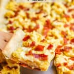 A wooden spatula lifting a slice of egg and bacon breakfast pizza from a sheet pan with a text overlay on the photo