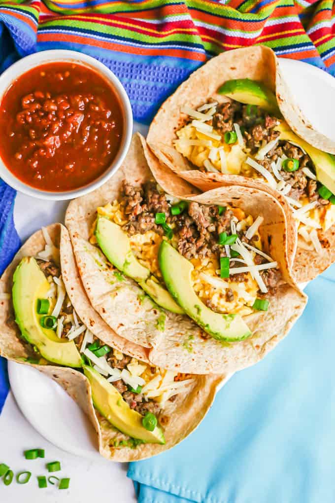 A platter with three breakfast tortillas with eggs, sausage and cheese and a bowl of salsa nearby