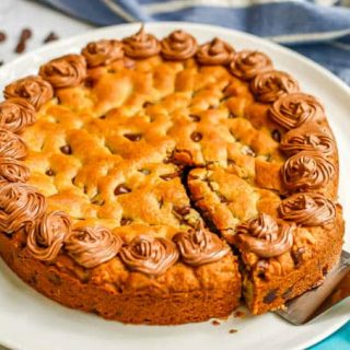 A pie cutter pulling a piece of chocolate chip cookie cake from a white platter