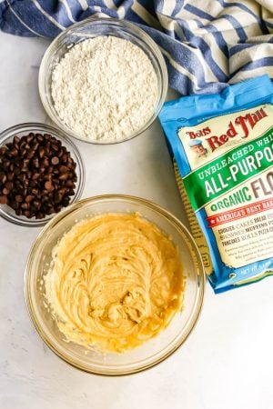 Ingredients for chocolate chip cookie cake laid out in glass bowls with a blue striped towel to the back