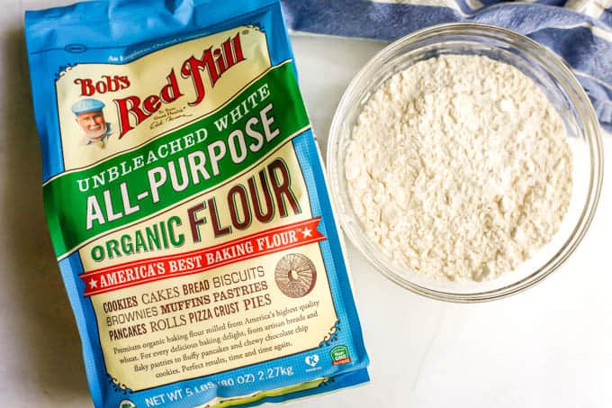 A bag of Bob's Red Mill unbleached white all-purpose flour beside a clear glass bowl of flour