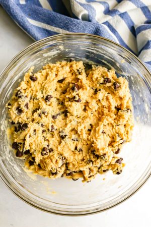 Chocolate chip cookie dough in a clear glass bowl with a blue striped towel to the side