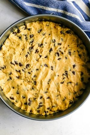 Chocolate chip cookie dough pressed into a springform pan before being baked