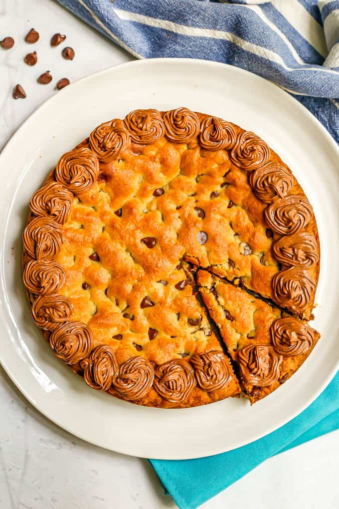 A homemade cookie cake on a white platter with one piece sliced