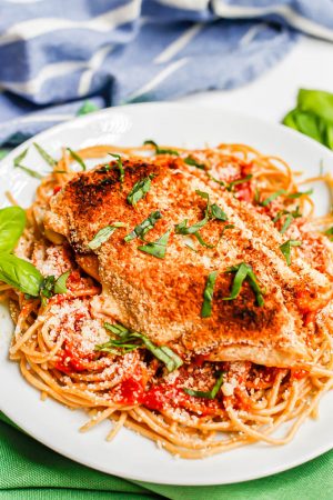 A broiled and browned chicken Parm cutlet served over spaghetti with basil sprinkled on top