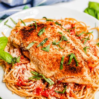 A broiled and browned chicken Parm cutlet served over spaghetti with basil sprinkled on top