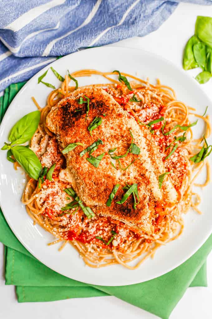 A crunchy chicken cutlet with marinara and mozzarella served on a white dinner plate with spaghetti noodles and fresh basil
