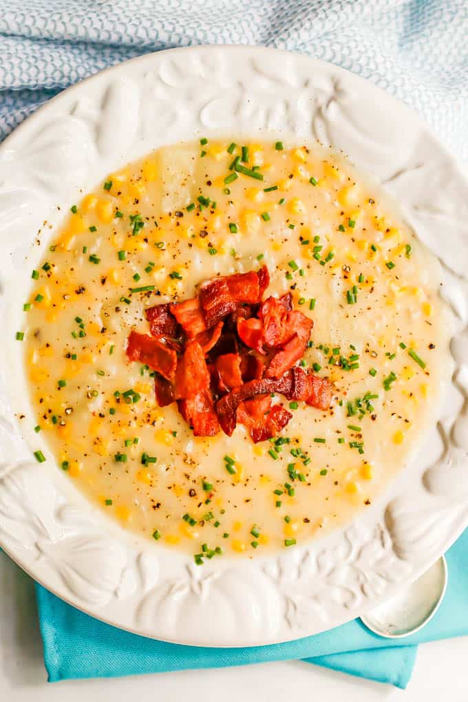 Creamy corn chowder served in a large white soup bowl with bacon and chives on top