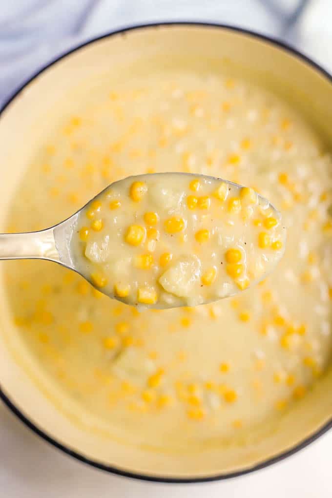 A silver serving spoon lifting a scoop of corn chowder from a large purple pot
