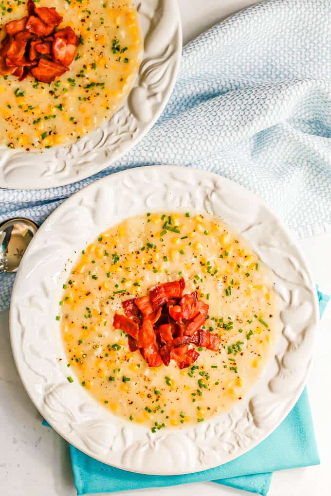 Two soup bowls with corn and potato chowder topped with bacon and chives