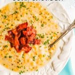 Corn chowder with bacon and chives served in an white bowl with a spoon resting in it and a text overlay on the photo
