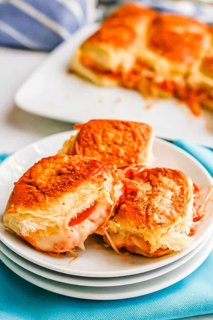 A small plate with three pizza sliders on it and a larger platter of sliders in the background