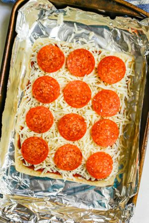 Pepperoni pizza sliders being assembled in a foil lined baking sheet
