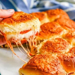 A hand picking up a pizza slider with pepperoni and melty mozzarella cheese
