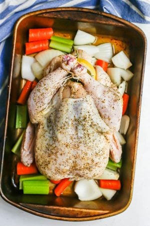 Overhead shot of a trussed and seasoned whole chicken on a bed of vegetables in a pan before being cooked