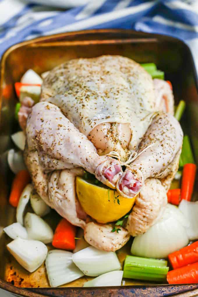 A trussed and seasoned whole chicken stuffed with lemon and thyme on a bed of vegetables in a pan before being cooked