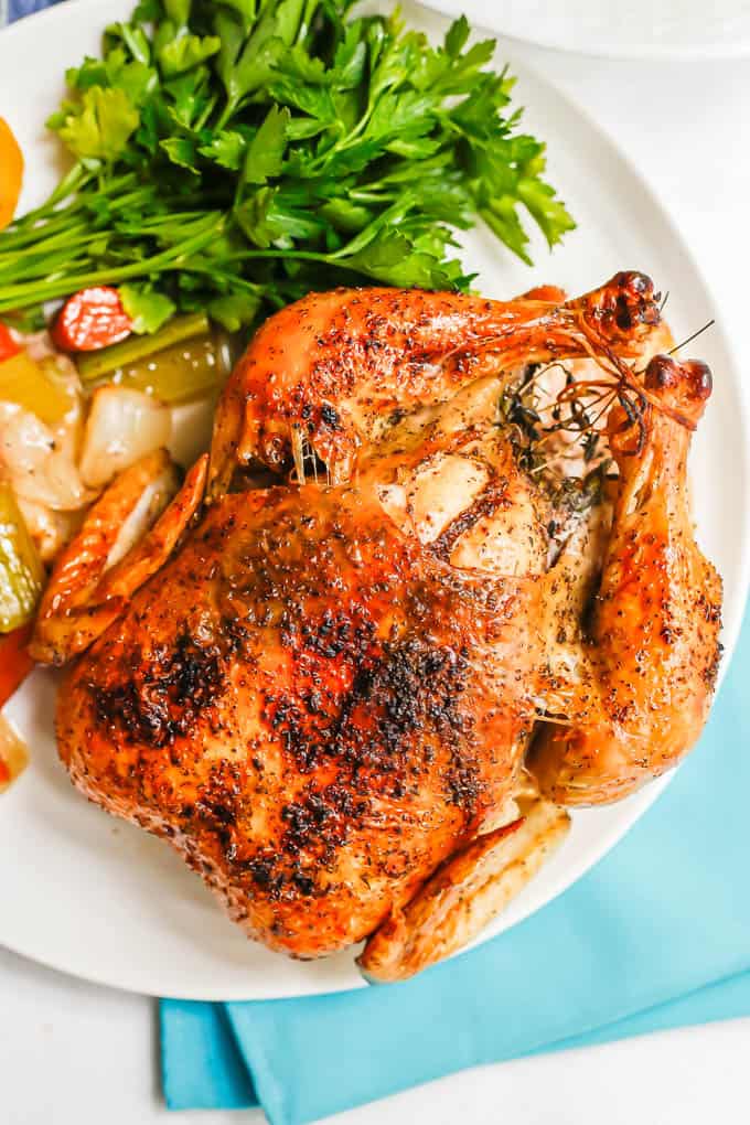 Close up of an oven roasted chicken served on a large white platter with a bunch of parsley to the side