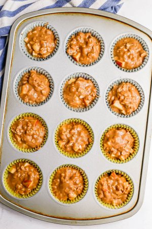Whole grain apple oat muffins in liners in a muffin tin before being baked