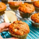 A hand about to pick up a whole grain apple cider muffin from a cooling rack with a text overlay on the photo