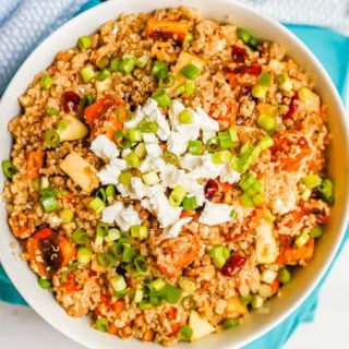 A bowl of quinoa salad with sweet potatoes, apples, pecans, dried cranberries and topped with feta cheese and green onions