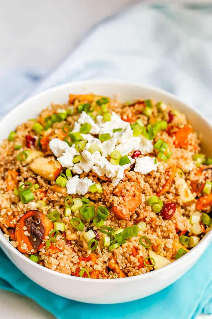A quinoa vegetable salad with sweet potatoes, apples, dried cranberries, pecans and feta cheese and green onions on top
