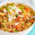 A large white bowl with a grain and veggie mix of quinoa, sweet potatoes, apples, feta cheese and green onions with a spoon resting in the bowl and a text box on the photo.