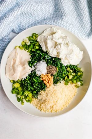 A large white bowl with layered ingredients for making a healthy spinach dip